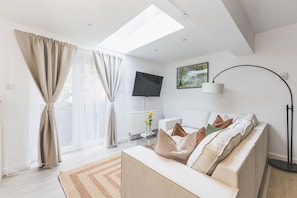 Ein modernes Wohnzimmer mit einer Couch, einem Flachbildfernseher, einer Stehlampe und einem Gemälde an der Wand.