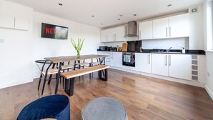 A modern kitchen with white cabinets, a wooden dining table, and a bench. - Modern 3beds 3baths in Hackney (London)