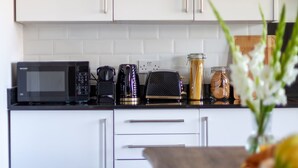 A modern kitchen with white cabinets, a microwave, a coffee maker, and a toaster. - Modern 3beds 3baths in Hackney (London)