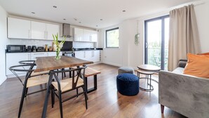 A modern kitchen with white cabinets, a wooden dining table, and a gray sofa. - Modern 3beds 3baths in Hackney (London)