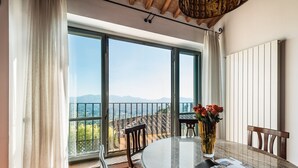 A dining area with a table, chairs, a vase with flowers, and a view of the mountains through large windows. - Panoramic Appartment With Garden (Capannori)