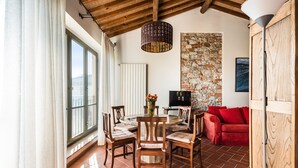 A dining area with a round table, chairs, a red sofa, a stone wall, and a wooden ceiling. - Panoramic Appartment With Garden (Capannori)