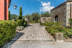 A stone pathway leading to a stone building with a door and window, surrounded by greenery and a clear sky. - Panoramic Appartment With Garden (Capannori)