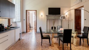 A modern kitchen with a dining area, granite countertop, and a TV mounted above the fireplace. - Tintoretto Superior Apartment in Historic Villa (Capannori)