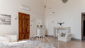 A bedroom with a bed, a wooden wardrobe, a white dresser, a white armchair, a fireplace, and a painting on the wall. - Tintoretto Superior Apartment in Historic Villa (Capannori)