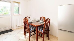 A dining area with a round table set for four, wooden chairs with striped cushions, a white refrigerator, and a window with blinds. - Omega Hanwell 2nd Floor Ensuite Free Parking (London)