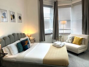 Ein Hotelzimmer mit einem Bett, einer Couch, einer Lampe und einem Fenster mit Vorhängen.