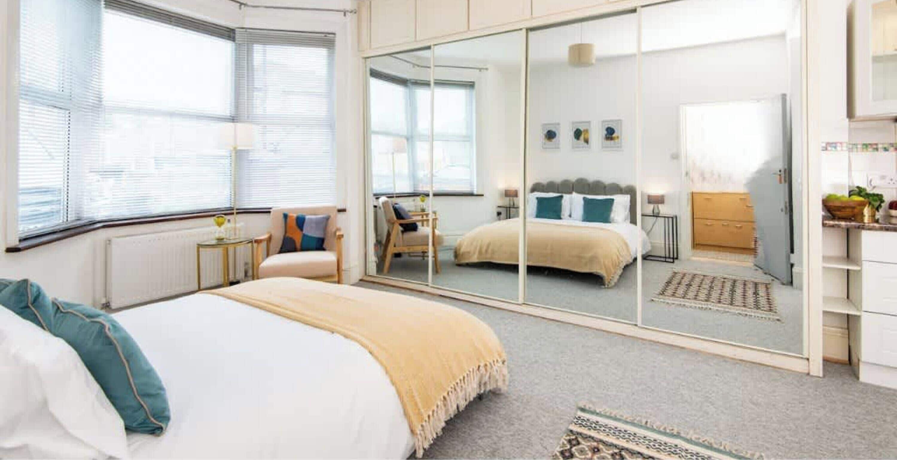 A bedroom with a bed, a wardrobe, a mirror, and a window.