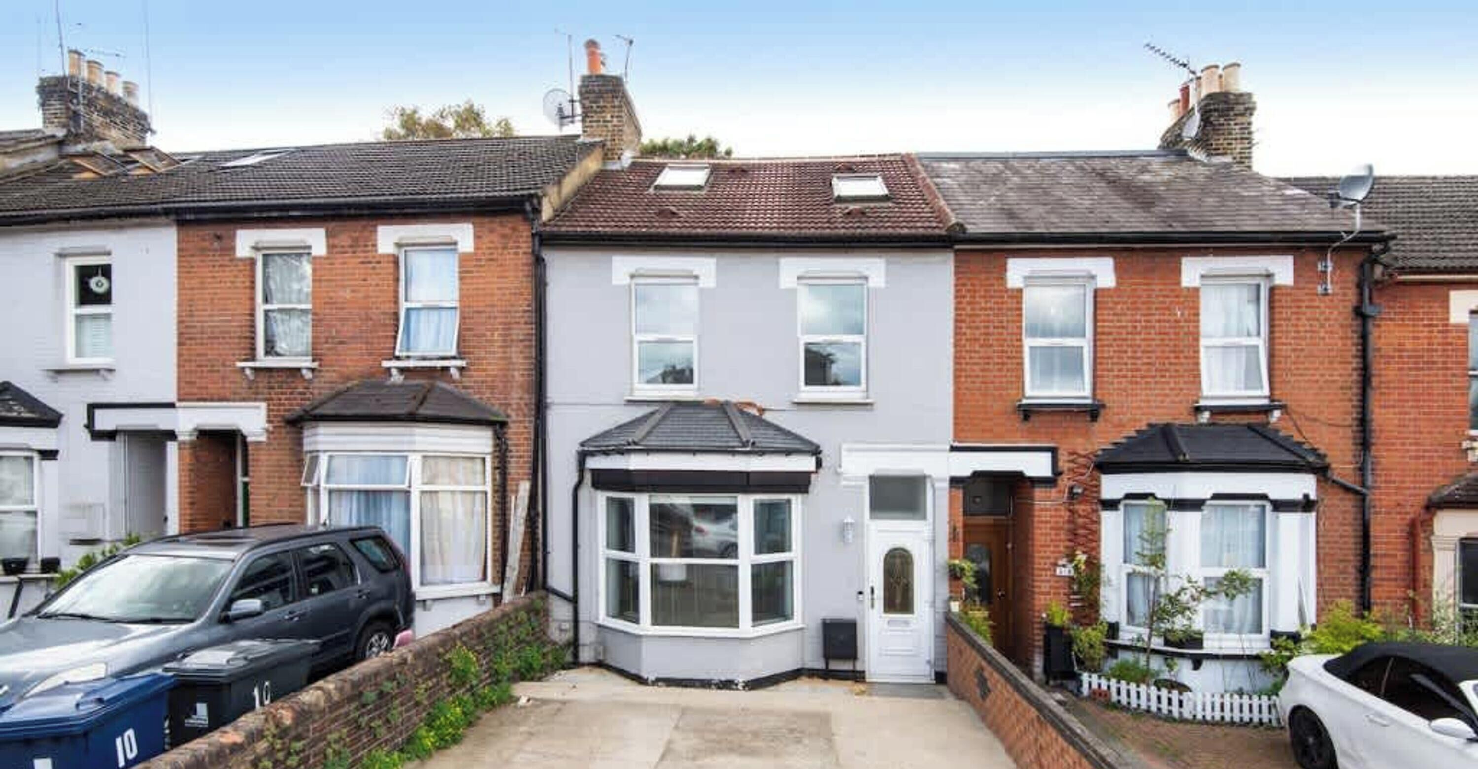 A row of terraced houses with a garage on the left, a bay window on the second house, and a white picket fence on the right.