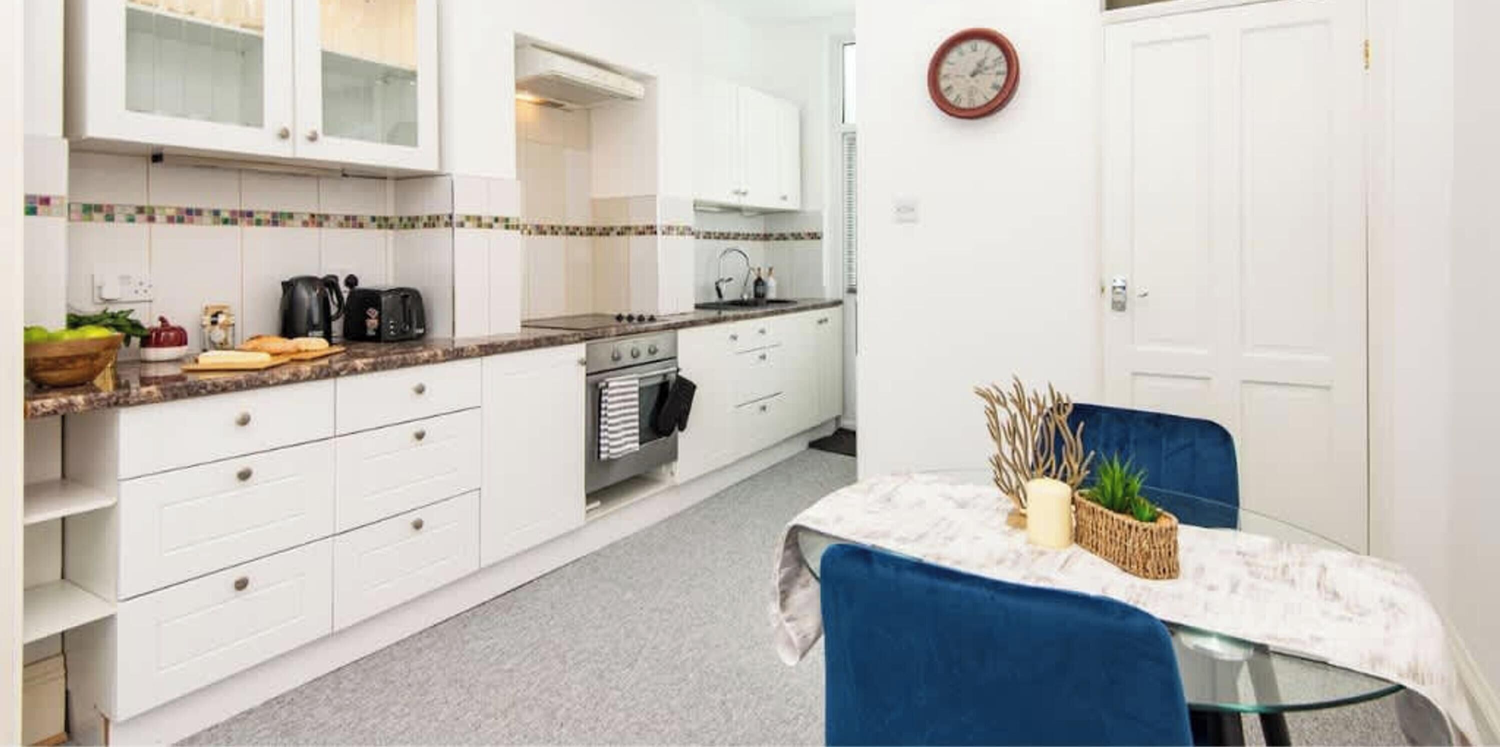 A compact kitchen with white cabinets, a stove, and a dining area with a table and chairs.