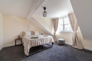 A bedroom with a bed, bedside tables, a hanging light fixture, a window with curtains, and a view of the outdoors. - Lovely House in Stratford (London)