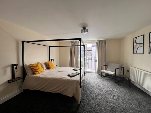 A four-poster bed with a headboard, a bedside table, a chair, and a radiator. - Lovely House in Stratford (London)