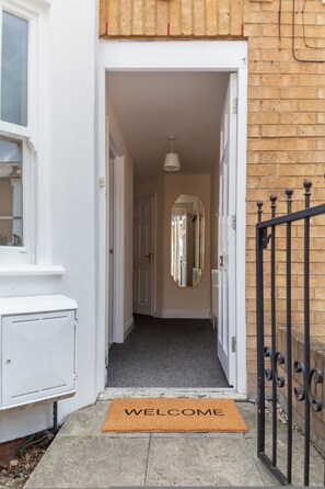 A narrow hallway with a welcome mat, a door, and a mirror on the wall. - Lovely House in Stratford (London)
