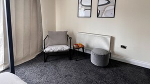 Et værelse med en stol, en radiator, et lille bord med frugt og to billeder hængt på væggen.