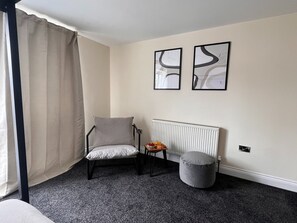 A room with a chair, a radiator, a small table with fruit, and two wall-mounted pictures. - Lovely House in Stratford (London)