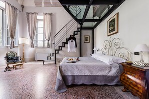 A bedroom with a bed, a chair, a dresser, a lamp, a window with curtains, a staircase, and a framed picture on the wall. - Raffaello Comfort Apartament Villa Guinigi (Capannori)
