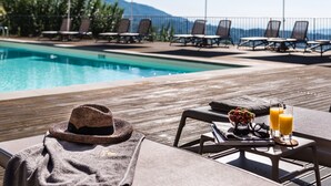 Un área junto a la piscina con sillones de descanso, sombrillas y una mesa con sombrero, gafas de sol y bebidas.