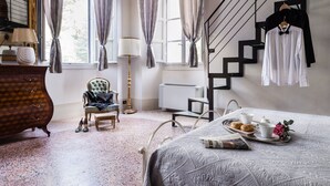 Un dormitorio con cama, cómoda, silla, lámpara, radiador, escalera y ventana con cortinas.