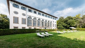 Un edificio grande y blanco con múltiples ventanas y una escalera que lleva a un balcón. Varias sillas de descanso están dispuestas en filas sobre un césped.