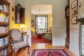 A room with a wooden floor, a patterned rug, a bookshelf, a green armchair, a white sofa, and a large wooden cabinet. - Luxury 1820s Georgian Home 5-min Walk to Station (London)