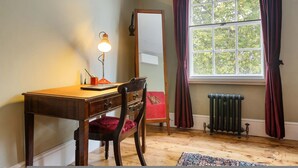 Ein Zimmer mit Holzschreibtisch, Stuhl, Spiegel, Heizkörper und einem fenster mit Vorhängen.