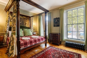 A four-poster bed with a red and white patterned bedspread, a large window with a view of trees, and a radiator on the floor. - Luxury 1820s Georgian Home 5-min Walk to Station (London)