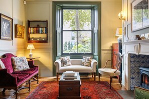 A cozy living room with a sofa, armchair, and a fireplace. - Luxury 1820s Georgian Home 5-min Walk to Station (London)