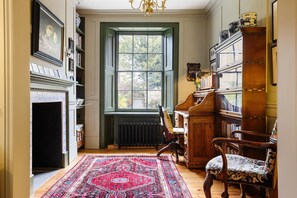 A room with a fireplace, a large window, a wooden chair, a bookshelf, and a patterned rug. - Luxury 1820s Georgian Home 5-min Walk to Station (London)