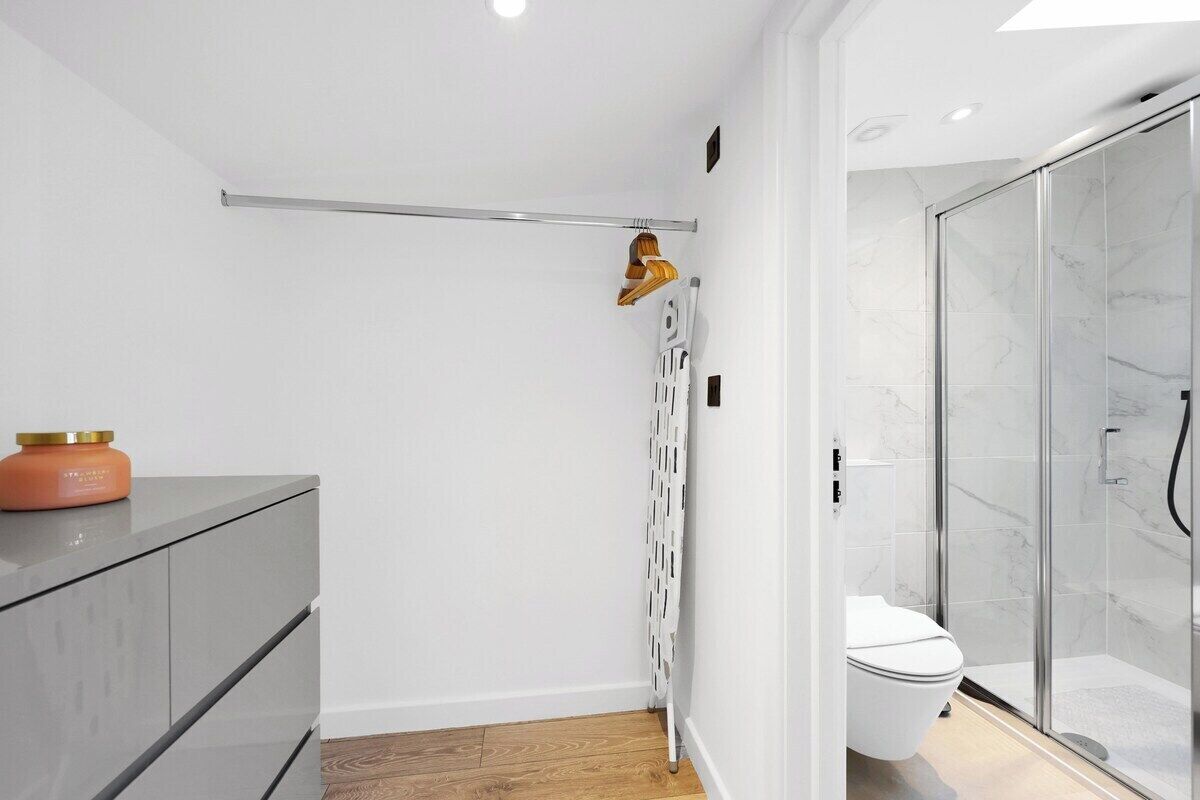 Une salle de bain moderne avec une douche à parois de verre, des toilettes blanches et un meuble gris agrémenté d’une bougie.