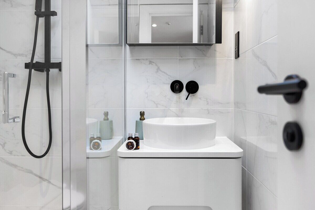 Un bagno moderno con un lavabo in marmo bianco, un soffione doccia manuale e un water con maniglia nera.