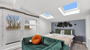 A bedroom with a skylight, a bed, a green sofa, and a wall with decorative plates. - Spacious Rooftop Studio Flat in London (London)