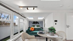 A modern room with a green sofa, a dining table with chairs, and a potted plant. - Spacious Rooftop Studio Flat in London (London)