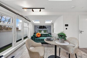 A modern room with a green sofa, a dining table with chairs, and a potted plant. - Spacious Rooftop Studio Flat in London (London)