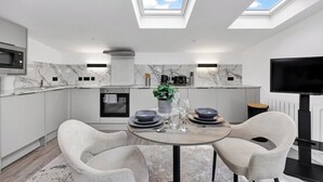 A modern kitchen with skylights, a dining area with a round table, and a flat-screen TV. - Spacious Rooftop Studio Flat in London (London)