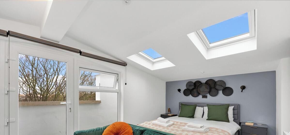 A bedroom with skylights, a bed with pillows, a bedside table, and a wall-mounted clock.