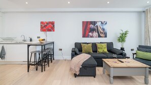 Un salon moderne avec un canapé, une table basse et un coin cuisine équipé d’un tabouret de bar.