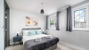 Une chambre à coucher comprenant un lit, une table de chevet, une lampe, un tableau, une fenêtre et des rideaux.