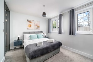 A bedroom with a bed, bedside table, lamp, artwork, window, and curtains. - 2bed 2bath Hendon - 3 min to Train - 65 Inch TV (London)