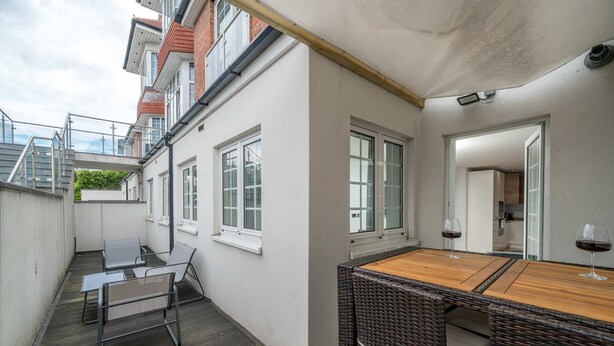Un balcon avec une table et des chaises, une terrasse en bois et une vue sur les bâtiments voisins.