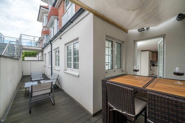 A balcony with a table and chairs, a wooden deck, and a view of adjacent buildings. - 2bed 2bath Hendon - 3 min to Train - 65 Inch TV (London)