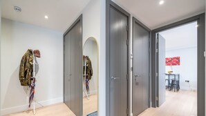 Un couloir avec des portes grises, un miroir, un porte-manteau avec une veste, et un tapis bleu.