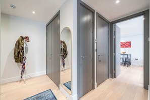 A hallway with grey doors, a mirror, a coat rack with a jacket, and a blue rug. - 2bed 2bath Hendon - 3 min to Train - 65 Inch TV (London)
