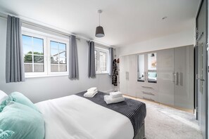 Ein Schlafzimmer mit Bett, Kleiderschrank, einem Fenster mit Vorhängen und einer Pendelleuchte.