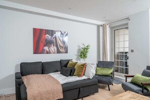 A modern living room with a grey sofa, a coffee table, and a large abstract painting on the wall. - 2bed 2bath Hendon - 3 min to Train - 65 Inch TV (London)