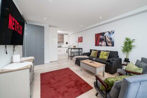 Ein modernes Wohnzimmer mit einer Couch, einem Couchtisch und einem roten Teppich. Ein Flachbildfernseher ist an der Wand befestigt.