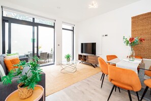En moderne stue med sofa, spisebord, stole, fjernsyn og et stort vindue.