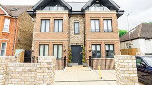 A two-story brick house with a central entrance, a small front garden, and a car parked in the driveway. - Modern Luxurious Retreat in Acton w Great Links (London)