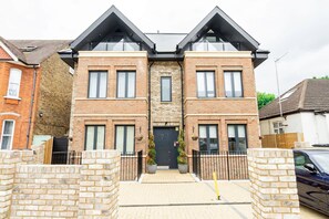 A two-story brick house with a central entrance, a small front garden, and a car parked in the driveway. - Modern Luxurious Retreat in Acton w Great Links (London)