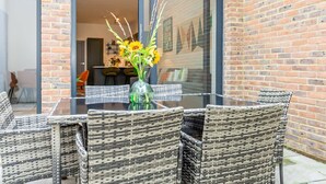 A glass table with wicker chairs, a vase with flowers, and a brick wall. - Modern Luxurious Retreat in Acton w Great Links (London)
