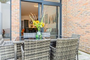 A glass table with wicker chairs, a vase with flowers, and a brick wall. - Modern Luxurious Retreat in Acton w Great Links (London)